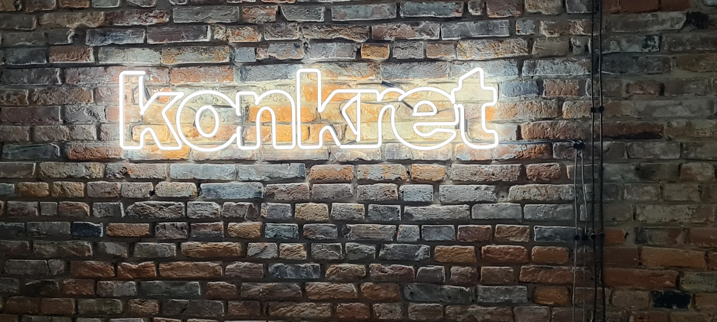 Biały neon „konkret” na ceglanej ścianie lokalu