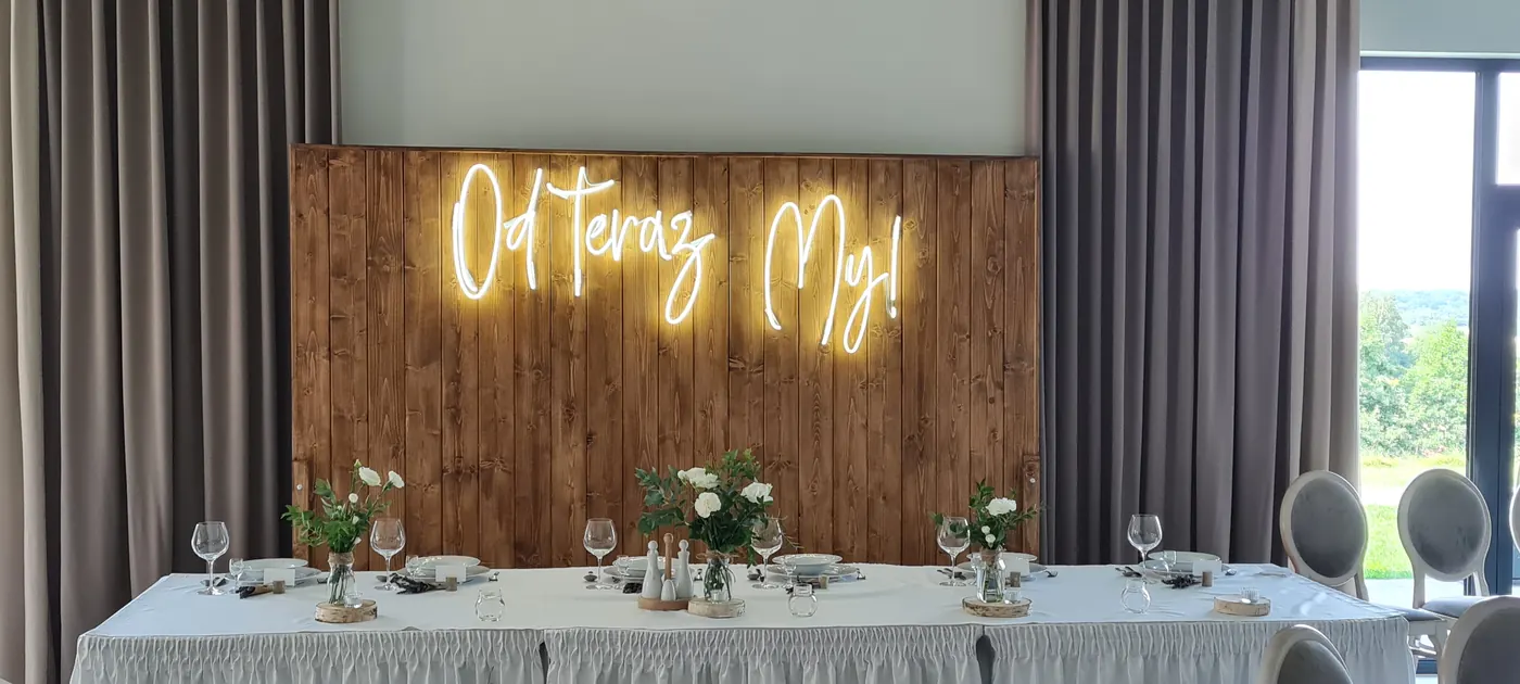 Neon „Od teraz My!” na drewnianej ścianie nad stołem młodej pary
